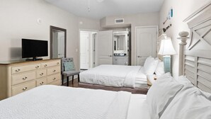 Habitación de hotel con dos camas, televisión, cómoda y ventilador de techo.
