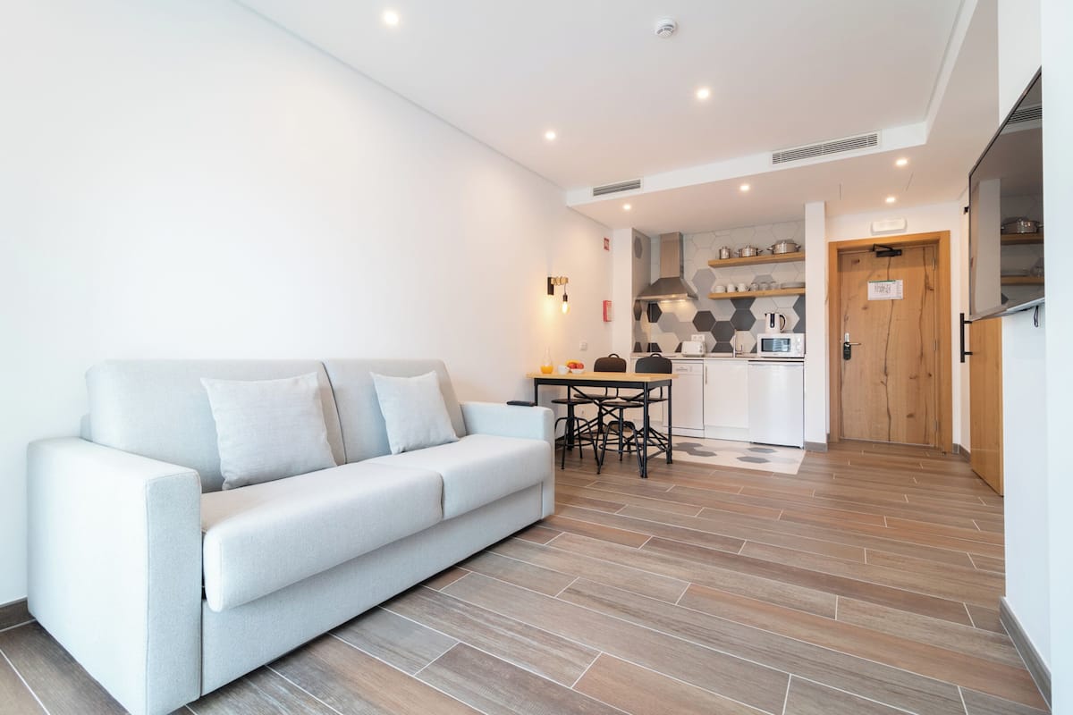 Una sala moderna con un sofá, una mesa de comedor con sillas, una zona de cocina con estufa y microondas, y una puerta de madera.