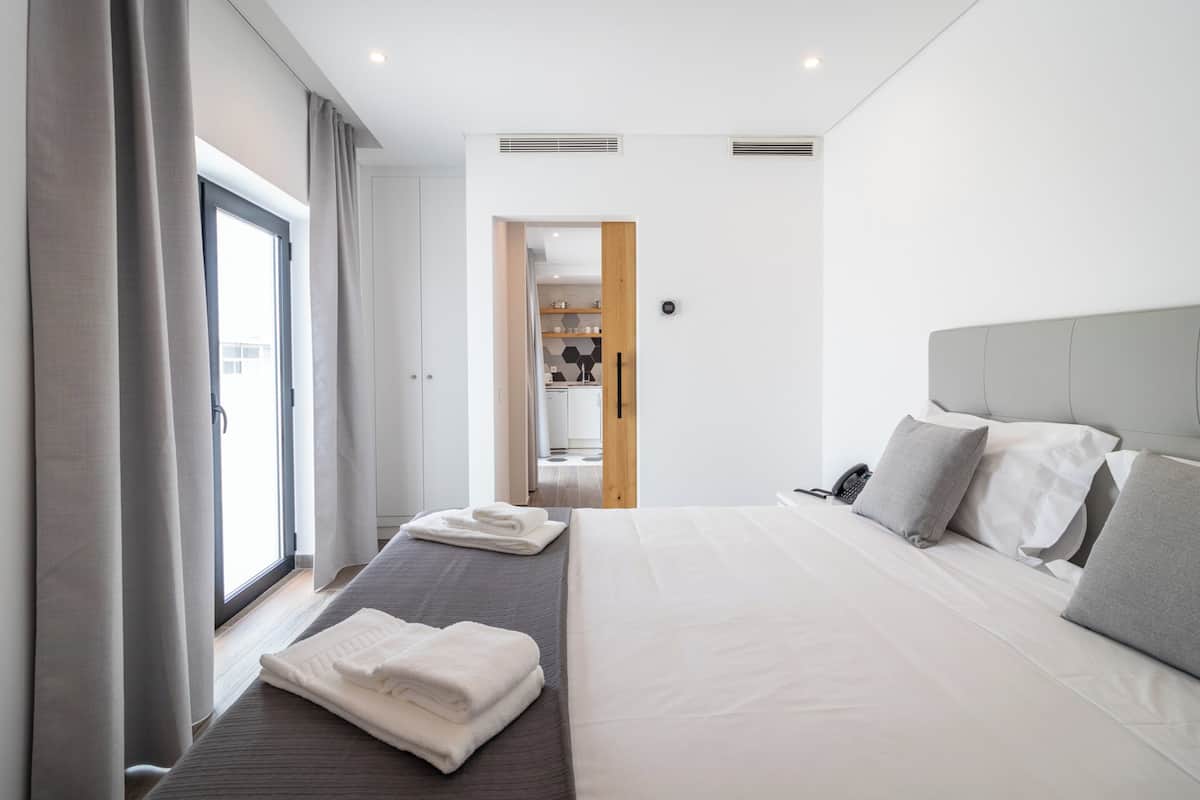 Una habitación de hotel moderna con una cama grande, una mesita de noche, un armario y un baño visible a través de una puerta abierta.