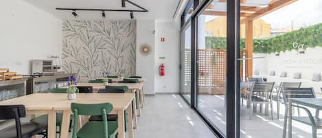 A modern hotel lobby with a long reception desk, green and black chairs, and a large window offering a view of the outdoor seating area.