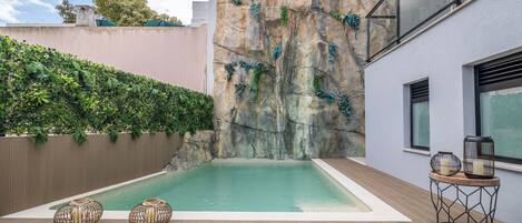 A swimming pool with a rock wall, wooden deck, and two decorative vases.