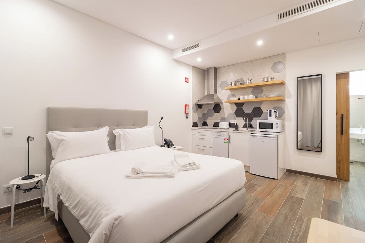 Habitación de hotel moderna con una cama grande, una kitchenette pequeña y un baño visible a través de una puerta abierta.