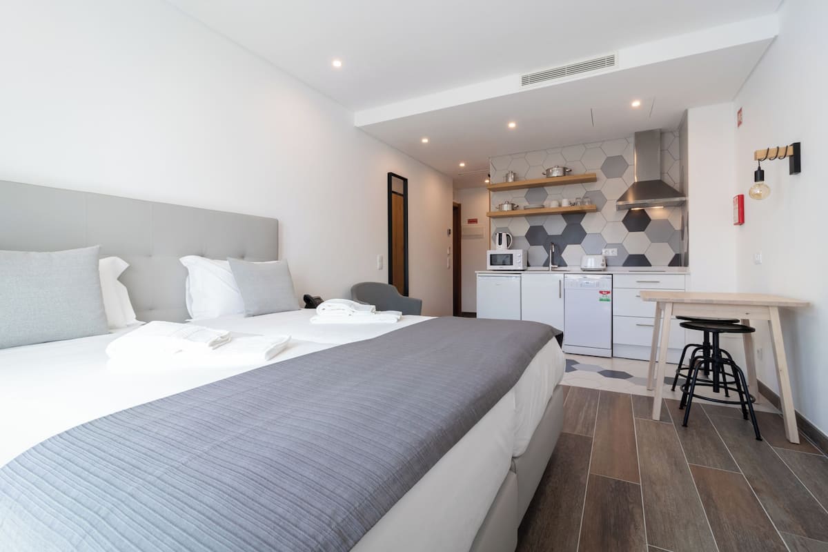 Una habitación de hotel moderna con una cama grande, una kitchenette pequeña y un escritorio con taburetes.