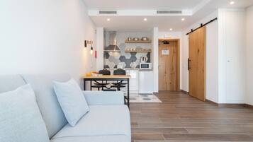 Uma sala de estar moderna com sofá, mesa de jantar e área de cozinha com micro-ondas e chaleira.