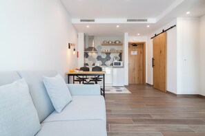A modern living room with a sofa, a dining table, and a kitchen area with a microwave and kettle.