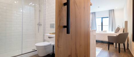 A modern bathroom with a glass shower enclosure, a white toilet, and a wooden door.