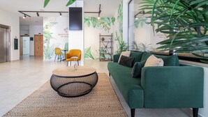 A modern lobby with a green sofa, yellow chairs, a round coffee table, and a large plant.