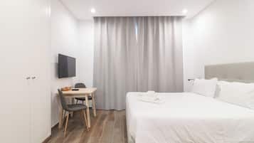 Habitación de hotel con cama, escritorio con silla, televisión de pantalla plana y ventana con cortinas.