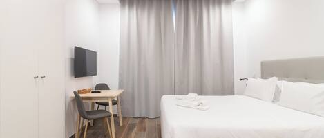 Une chambre d’hôtel comprenant un lit, un bureau avec une chaise, un téléviseur à écran plat et une fenêtre avec des rideaux.