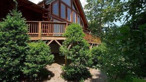 A wooden cabin with a balcony, surrounded by dense greenery. - Hickory Hideaway - 3 BR, 3 1/2 BA, Log Home, Stunning Views (Waynesville)