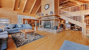 A spacious living room with a fireplace, wooden floors, and a staircase. - Hickory Hideaway - 3 BR, 3 1/2 BA, Log Home, Stunning Views (Waynesville)