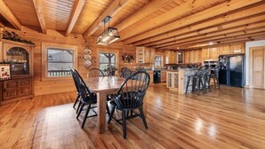 A spacious wooden cabin interior with a dining area, kitchen, and bar. - Hickory Hideaway - 3 BR, 3 1/2 BA, Log Home, Stunning Views (Waynesville)