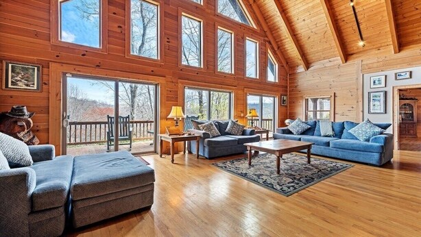 A spacious wooden cabin with large windows, a cozy living area with sofas and a coffee table, and a wooden ceiling. - Hickory Hideaway - 3 BR, 3 1/2 BA, Log Home, Stunning Views (Waynesville)