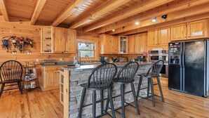 A wooden cabin interior with a kitchen, stone island, and bar stools. - Hickory Hideaway - 3 BR, 3 1/2 BA, Log Home, Stunning Views (Waynesville)