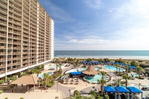Un hotel con varios balcones, zona de piscina con sombrillas y vistas a la playa.