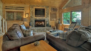 Ein gemütliches Blockhaus-Interieur mit Kamin aus Stein, Ledersofas und Holzbalkendecke.
