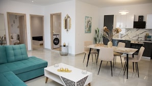 Una sala de estar moderna con un sofá color turquesa, una mesa de centro blanca y una zona de comedor con una mesa de mármol y sillas.