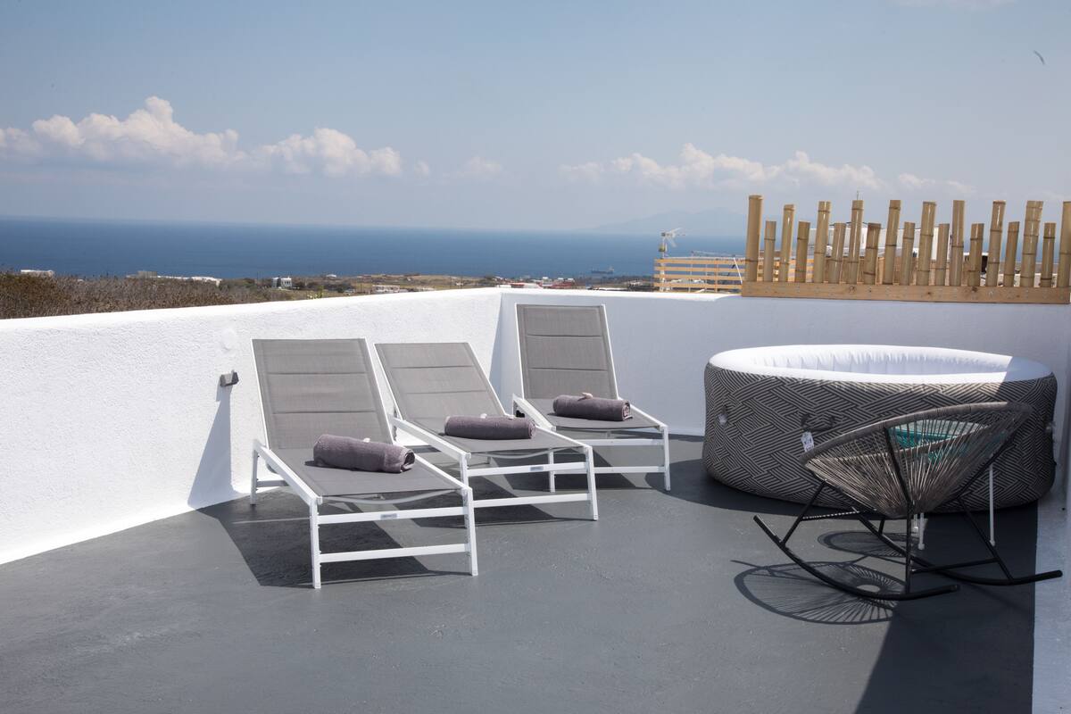 Eine Dachterrasse mit zwei Liegestühlen und einem Korbsessel, mit Blick auf die Küste.