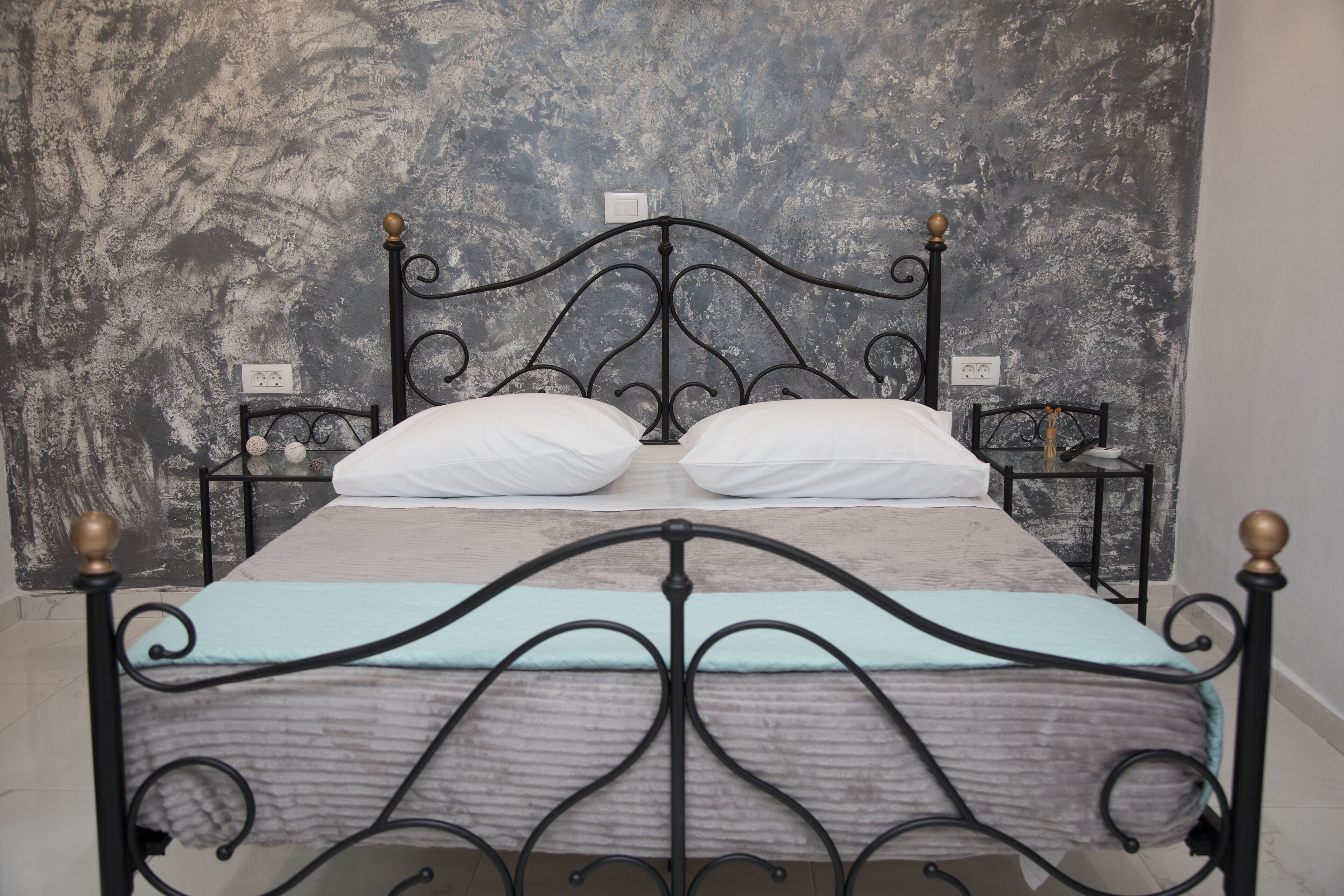A bed with a metal frame and two pillows, set against a textured wall.