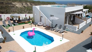 Un área de piscina moderna al aire libre con un flotador de flamenco rosa, sillas de descanso y vista al mar.