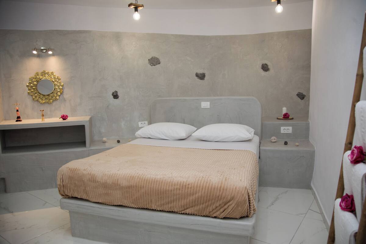 Ein modernes Schlafzimmer mit einem großen Bett, einem Nachttisch, einem Spiegel und einer Wand mit dekorativen Steinen.