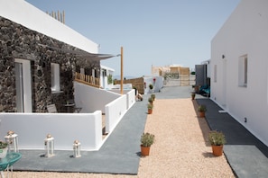 A narrow pathway flanked by white buildings with stone accents, leading to a gate. - Village Anto Fira (Santorini)