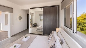 A modern bedroom with a large bed, a mirror, and a view of the outdoors. - Ayia Napa Bay View Villa 5 (Ayia Napa)