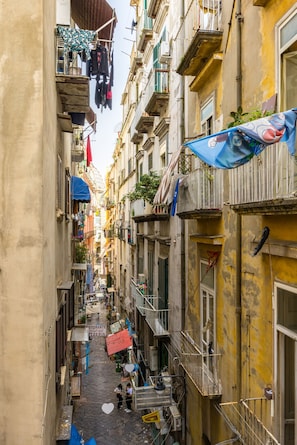 A narrow alleyway between buildings with balconies, some with clothes hanging, and a sign for a restaurant.