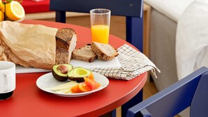 A breakfast setup with bread, avocado, tomatoes, and a glass of orange juice on a red table. - Studio Apartment for 4 (København)