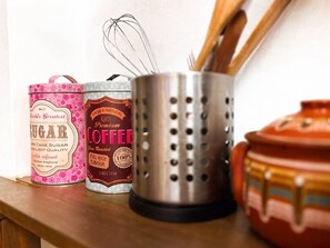 Three kitchen containers: a pink canister labeled "World's Greatest Sugar," a brown canister labeled "Fresh & Natural Premium Coffee," and a metal container with utensils. - Top Location | Kitchen | Outdoor Space (Sofia)