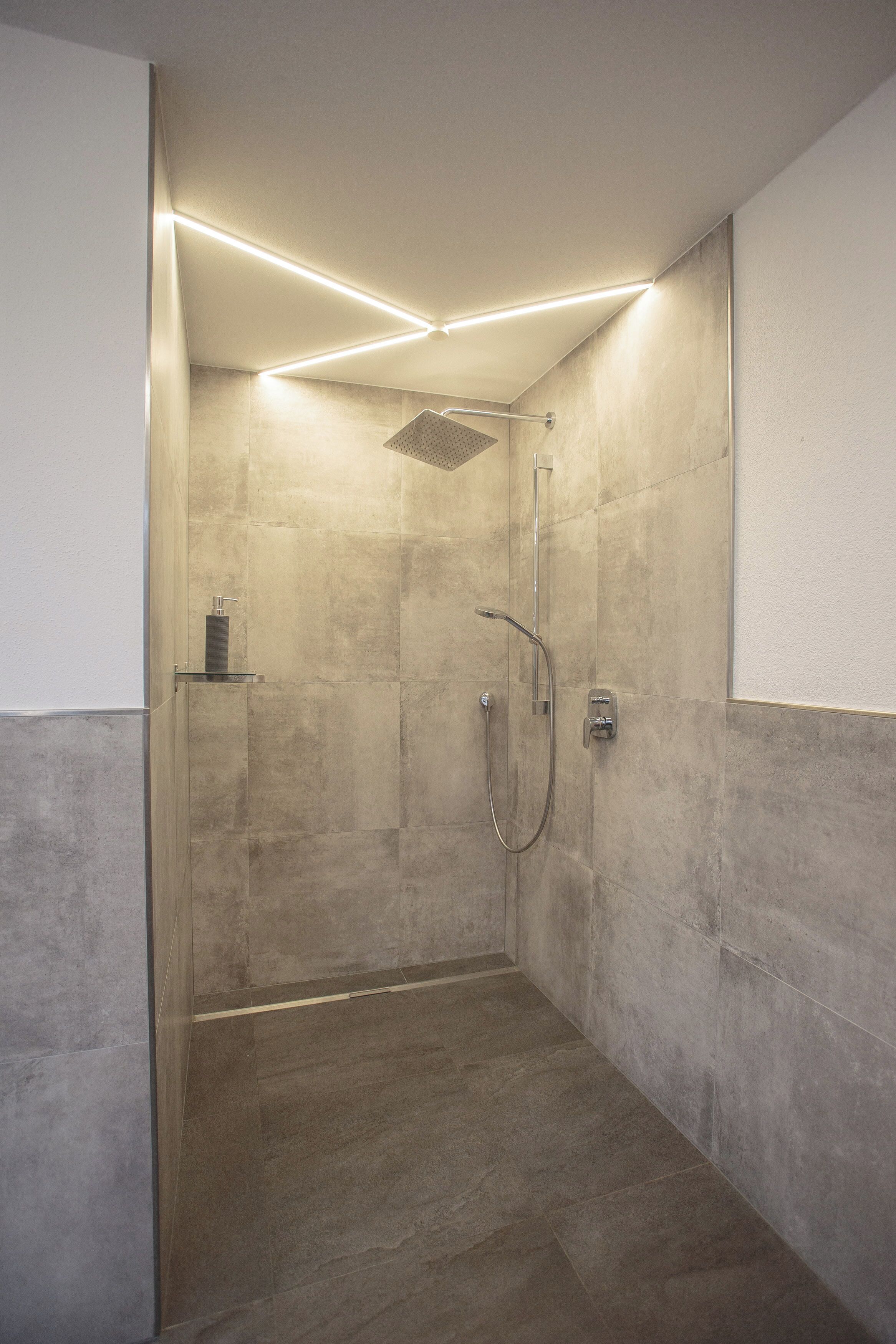 Een moderne douche met een glazen deur, een handdouche en een wandmengkraan.