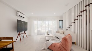 A modern living room with a flat-screen TV, a sofa, a wooden table, and a large window with sheer curtains. - Netflix, Brand new 4BR,Fast NBN,AC, Free Parking (Southport)