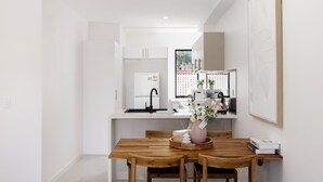 A modern kitchen with white cabinetry, a black faucet, and a wooden dining table with chairs. - Netflix, Brand new 4BR,Fast NBN,AC, Free Parking (Southport)