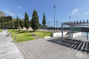 A sports facility with a wooden walkway, seating areas, and a fenced tennis court. - Home Azores - Pico do Salomão Poolside Retreat (Ponta Delgada)