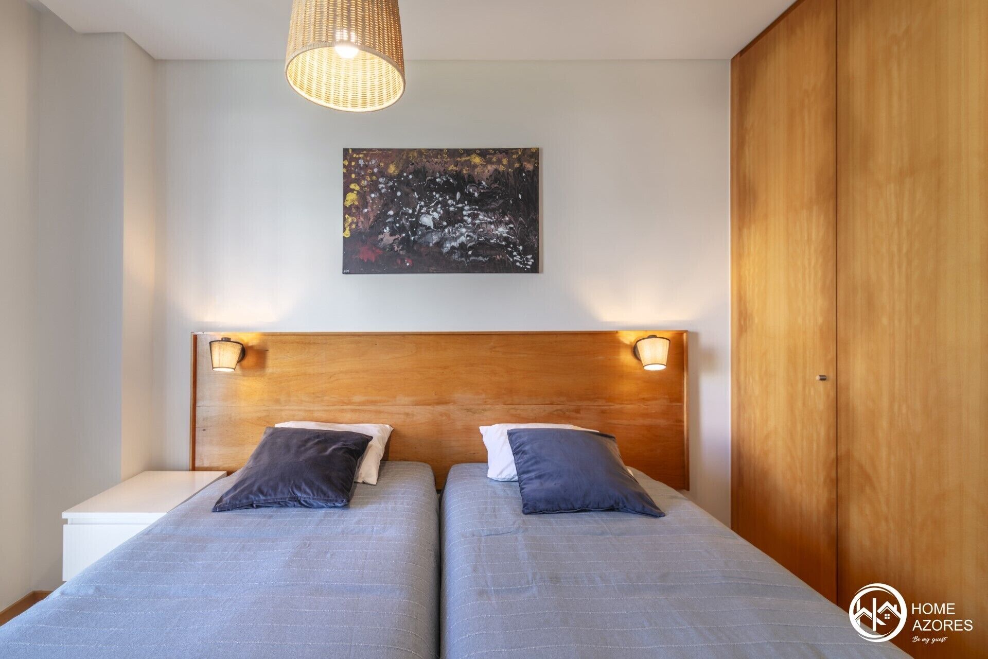 A bedroom with two beds, a wooden headboard, a painting on the wall, and a wardrobe.