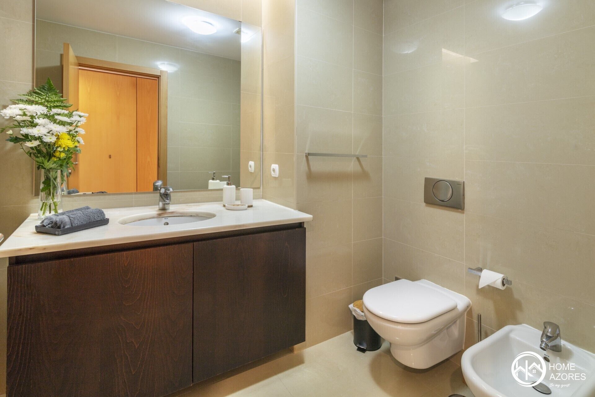 A modern bathroom with a wooden vanity, a sink, a toilet, and a bidet.