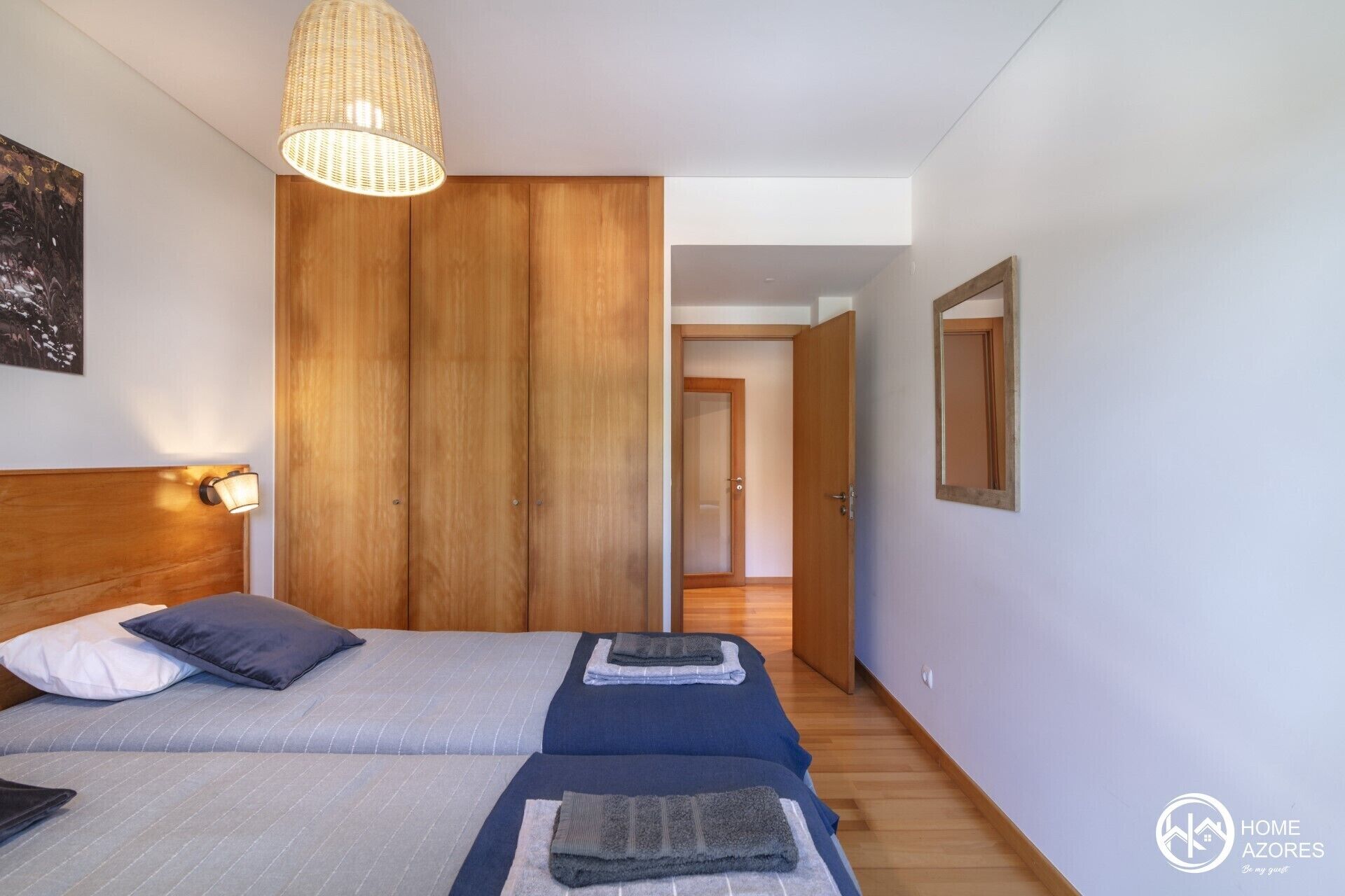 A bedroom with two beds, a wooden wardrobe, a hanging light fixture, and a mirror on the wall.