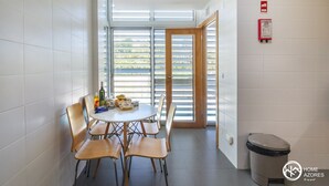 A dining area with a round table and four chairs, a trash bin, and a fire safety sign on the wall. - Home Azores - Pico do Salomão Poolside Retreat (Ponta Delgada)