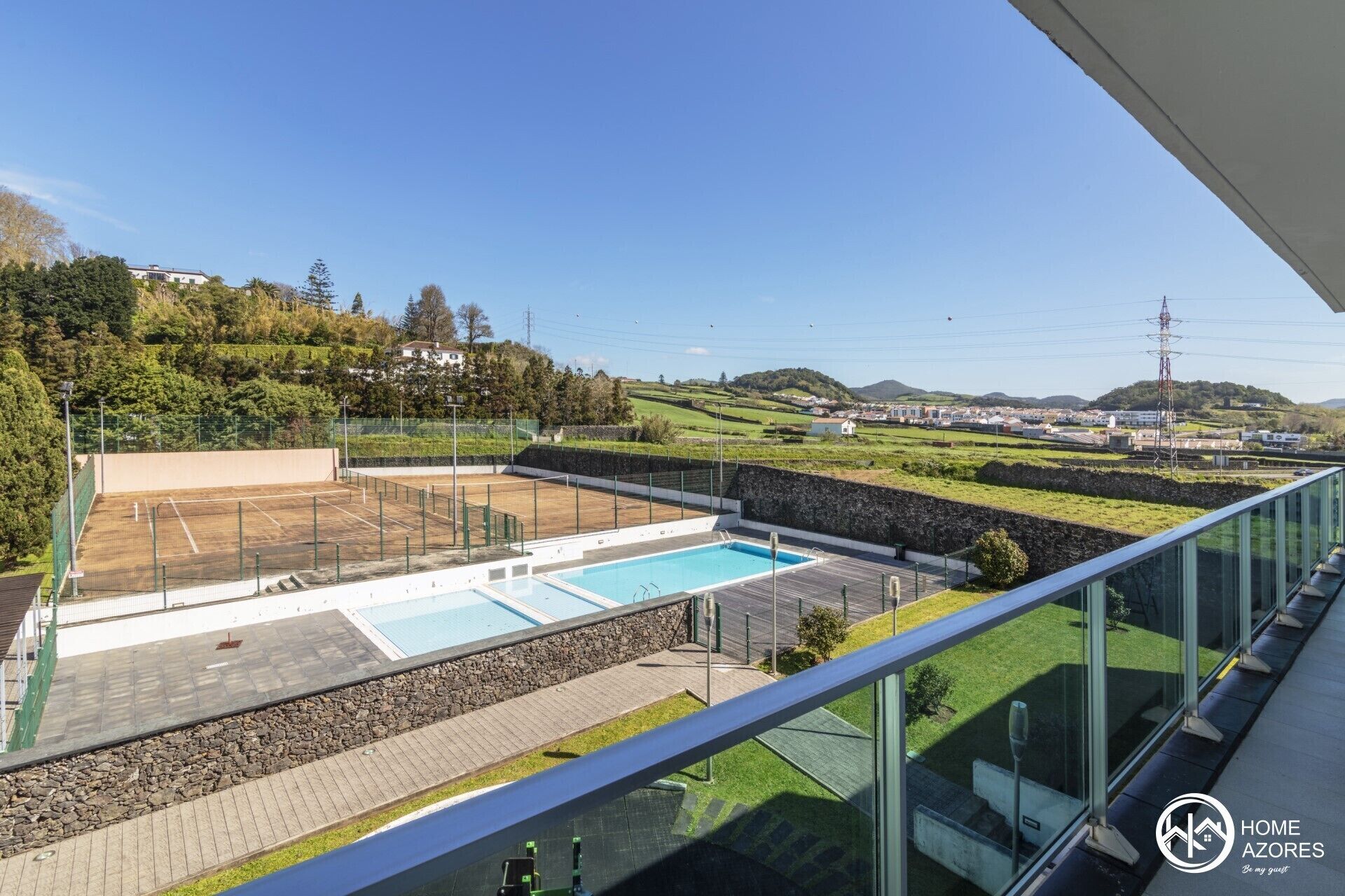 A residential property with a swimming pool, tennis court, and a view of the surrounding landscape.