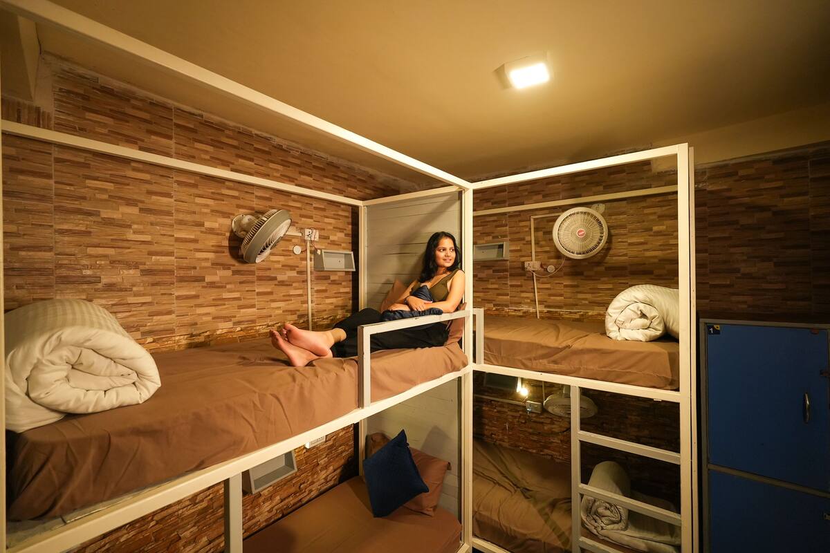 A dormitory room with bunk beds, a desk, a lamp, and a fan.