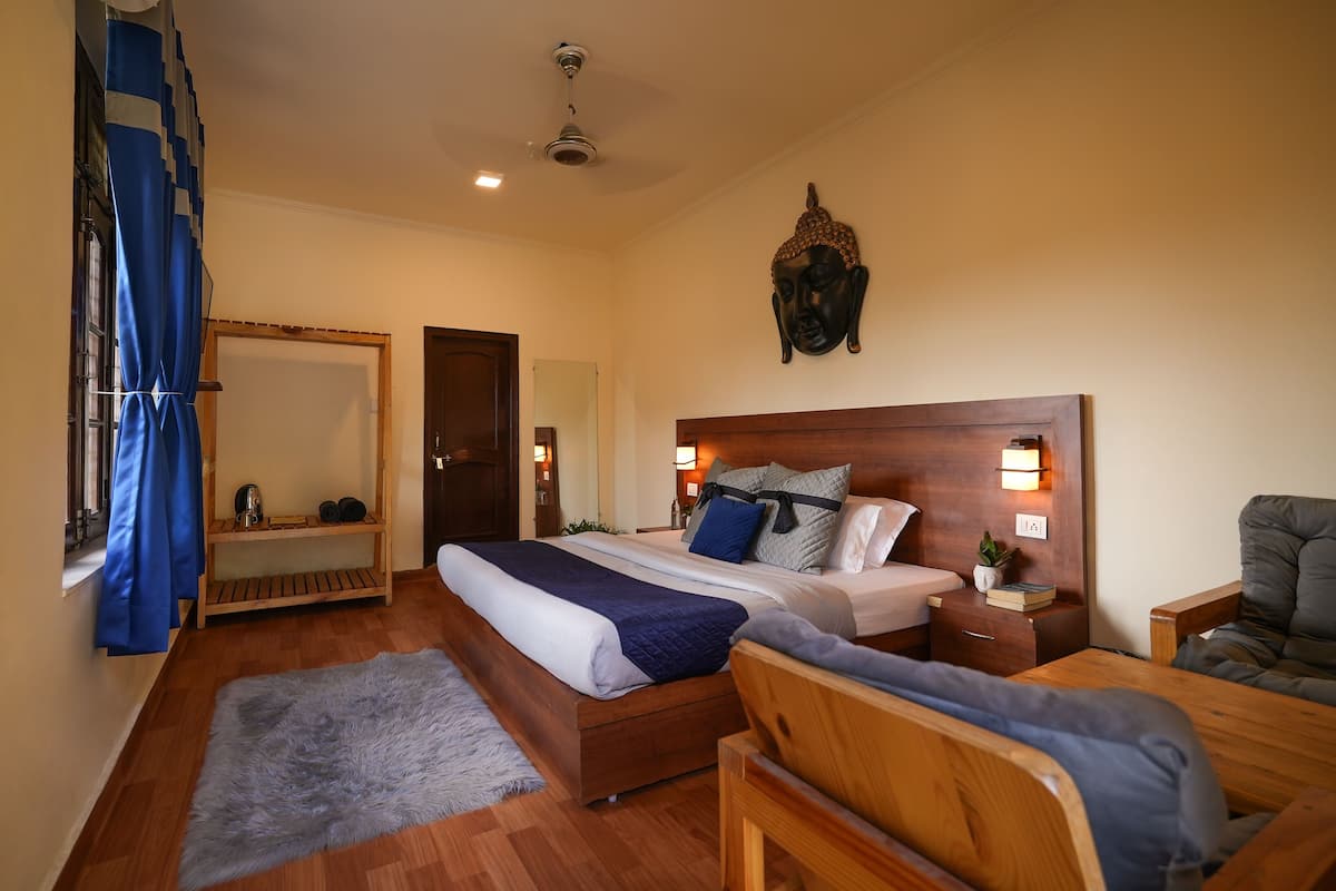 A bedroom with a large bed, a wooden headboard, a nightstand, a chair, a mirror, and a window with curtains.