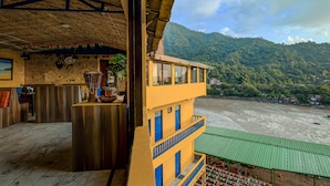 A hotel with a balcony overlooking a river and mountains. - Shalom Backpackers Rishikesh (Narendranagar)