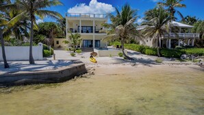 Una propiedad frente a la playa con piscina, palmeras y un edificio de dos pisos.