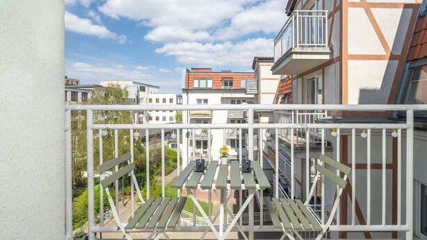 A balcony with a view of neighboring buildings, a table with chairs, and a small potted plant.