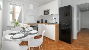 A modern kitchen with white cabinetry, a black refrigerator, and a dining area with white chairs and a table set for two.