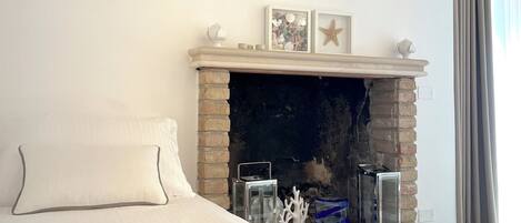 Un dormitorio con chimenea de ladrillo, televisor de pantalla plana montado encima y cama con ropa de cama blanca.