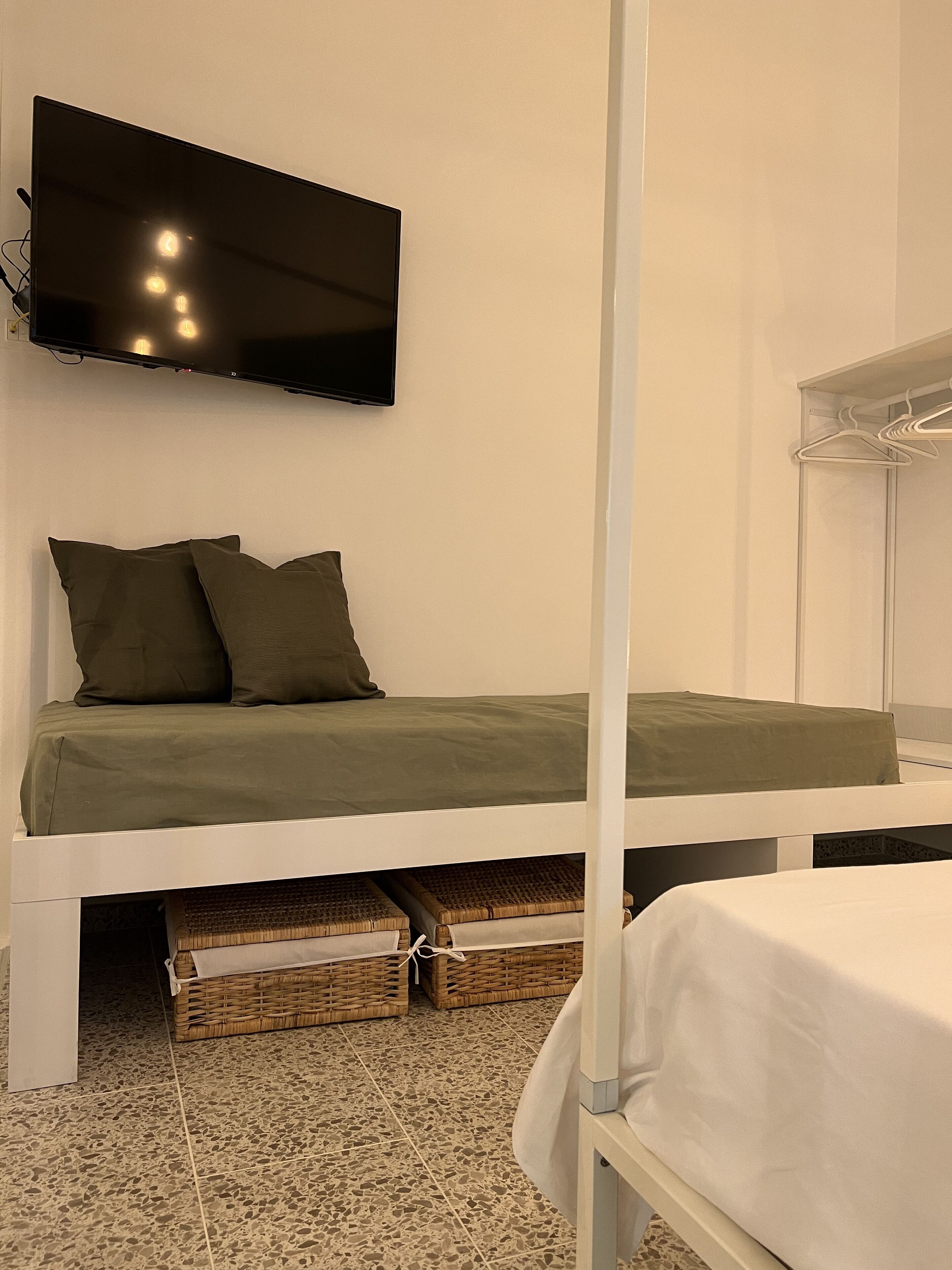 Un dormitorio con cama, televisor montado en la pared y cestas de almacenamiento debajo de la cama.