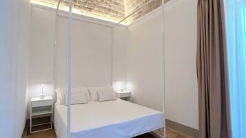 Une chambre à coucher avec un lit à baldaquin, des murs blancs, un plafond en briques et une fenêtre avec des rideaux.