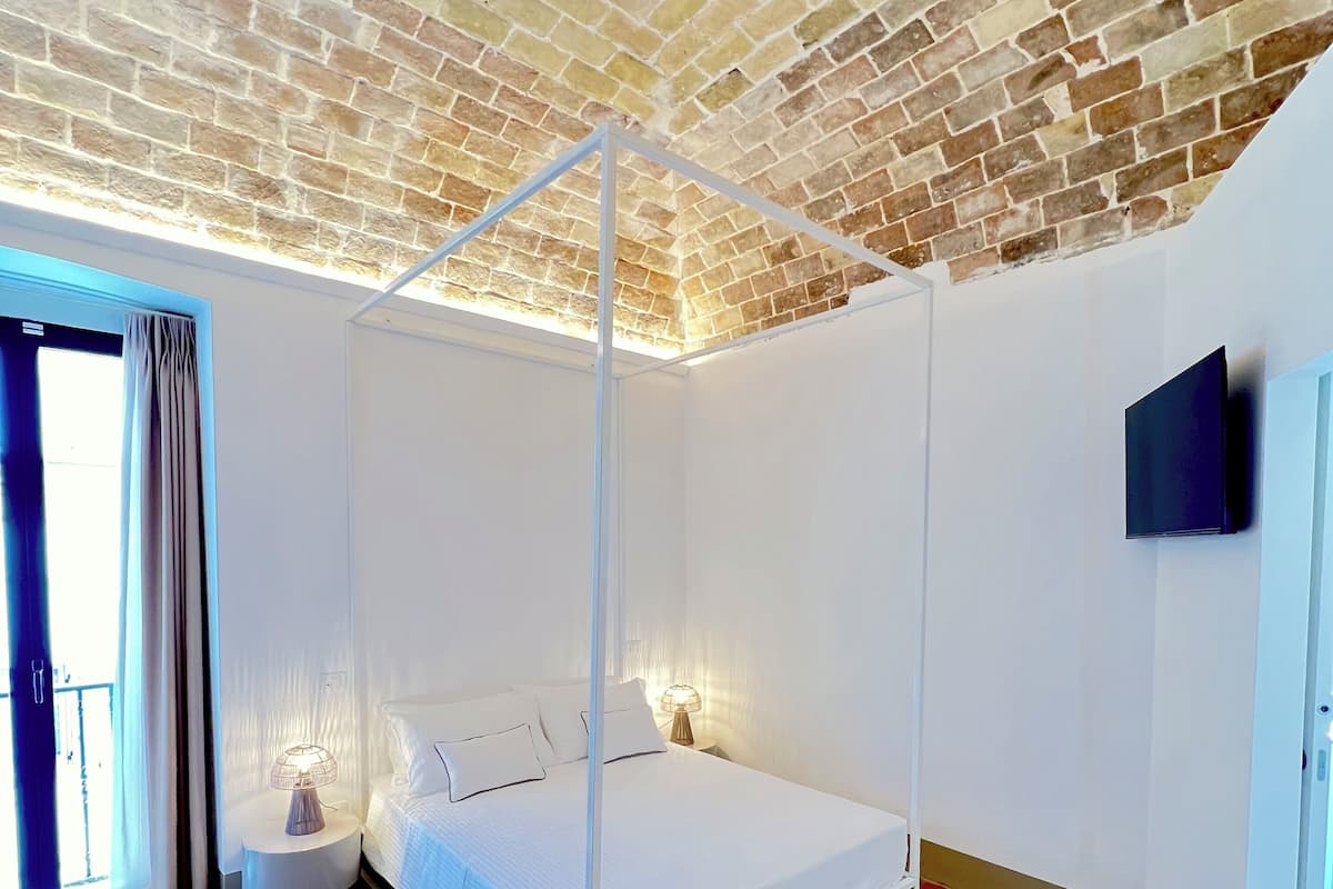 A bedroom with a four-poster bed, a TV mounted on the wall, and a brick ceiling.
