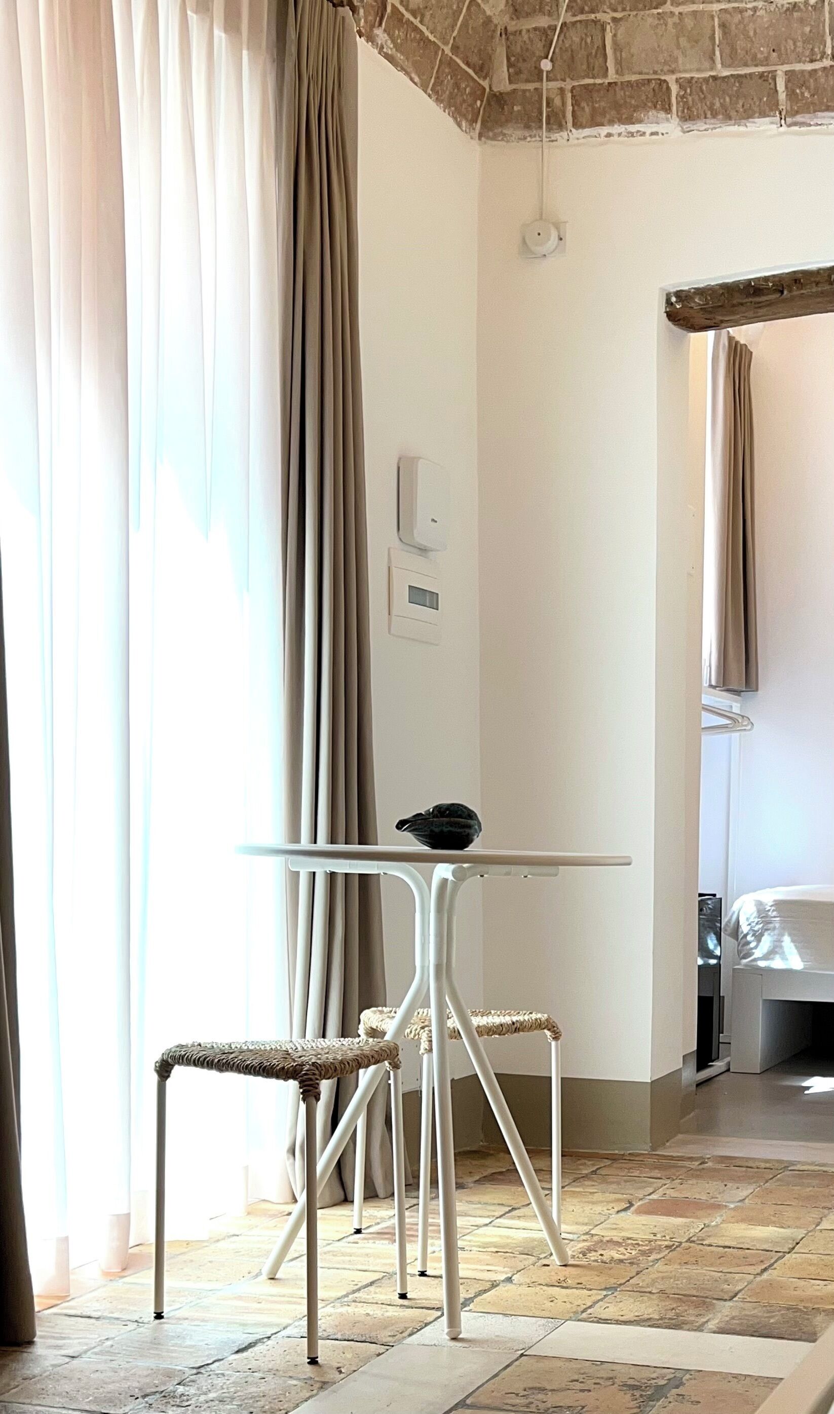 Quarto com uma mesa redonda, duas cadeiras de vime, piso de ladrilho e teto de tijolo.